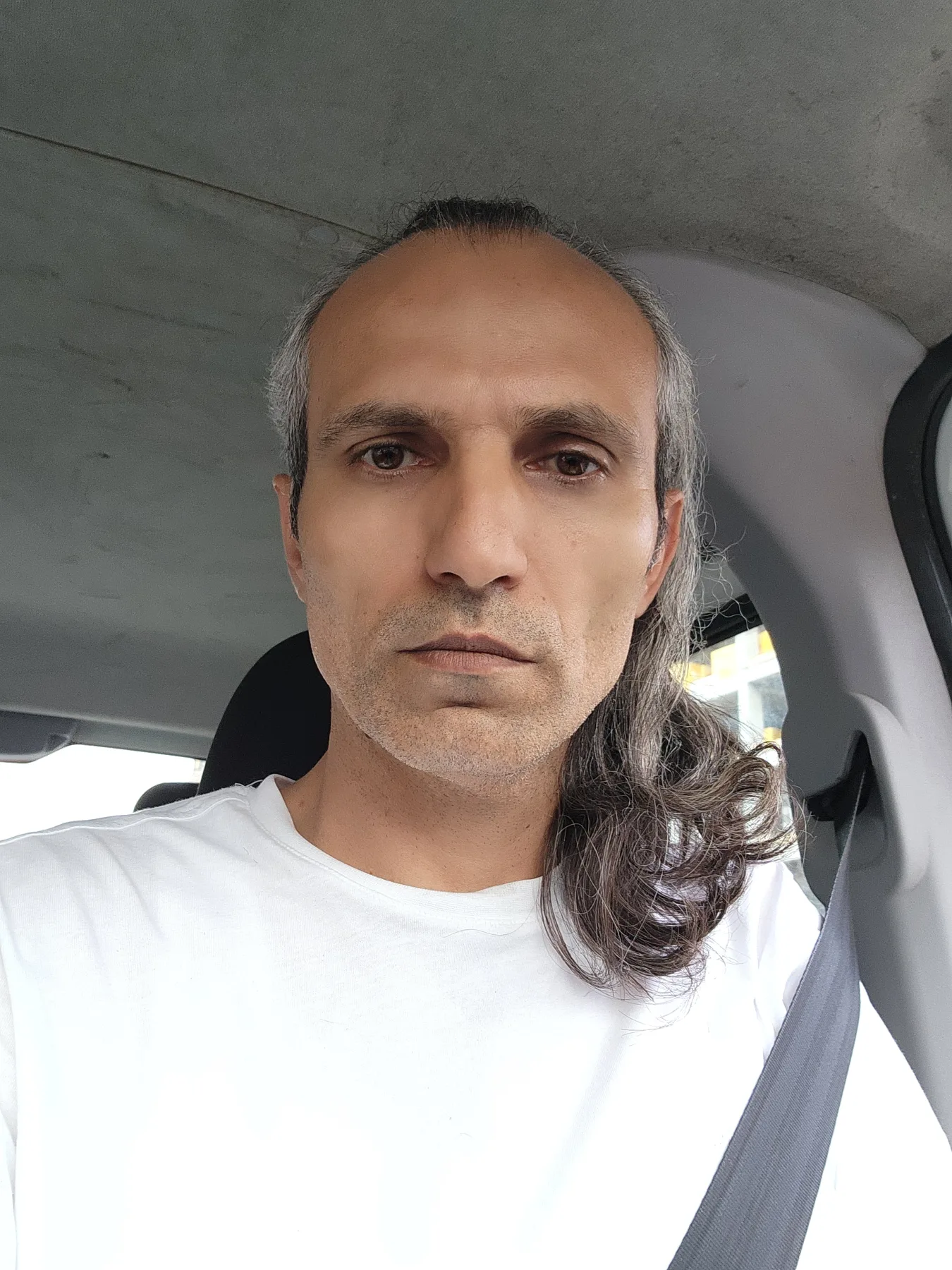 Galip Arduç, araç içinde beyaz tişörtü ve emniyet kemeriyle kameraya bakıyor.