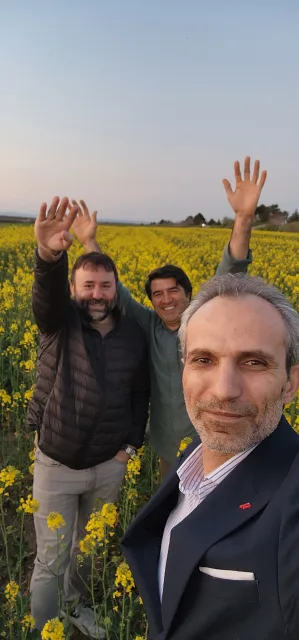 Galip Arduç’un fotoğraf arşivinden, sarı çiçeklerle kaplı bir tarlada el sallayan üç kişinin özçekimi.