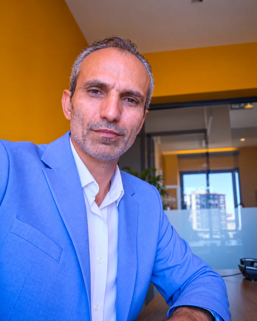 Mavi ceket ve beyaz gömlek giymiş Galip Arduç'un ofis ortamında kameraya kararlı bir şekilde baktığı portre fotoğrafı.