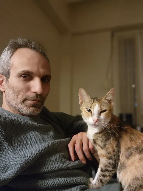 Galip Arduç'un evinde, gri kazağıyla otururken çok sevdiği, kahverengi, beyaz ve gri tonlarındaki kedisi Mia ile birlikte çekilmiş samimi hatıra fotoğrafı.