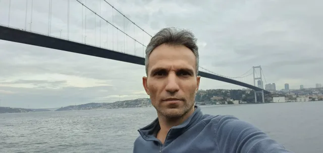 Galip Arduç’un İstanbul Boğazı ve köprü manzarası önünde, sakin ve kararlı duruşuyla çekilmiş açık hava portresi.