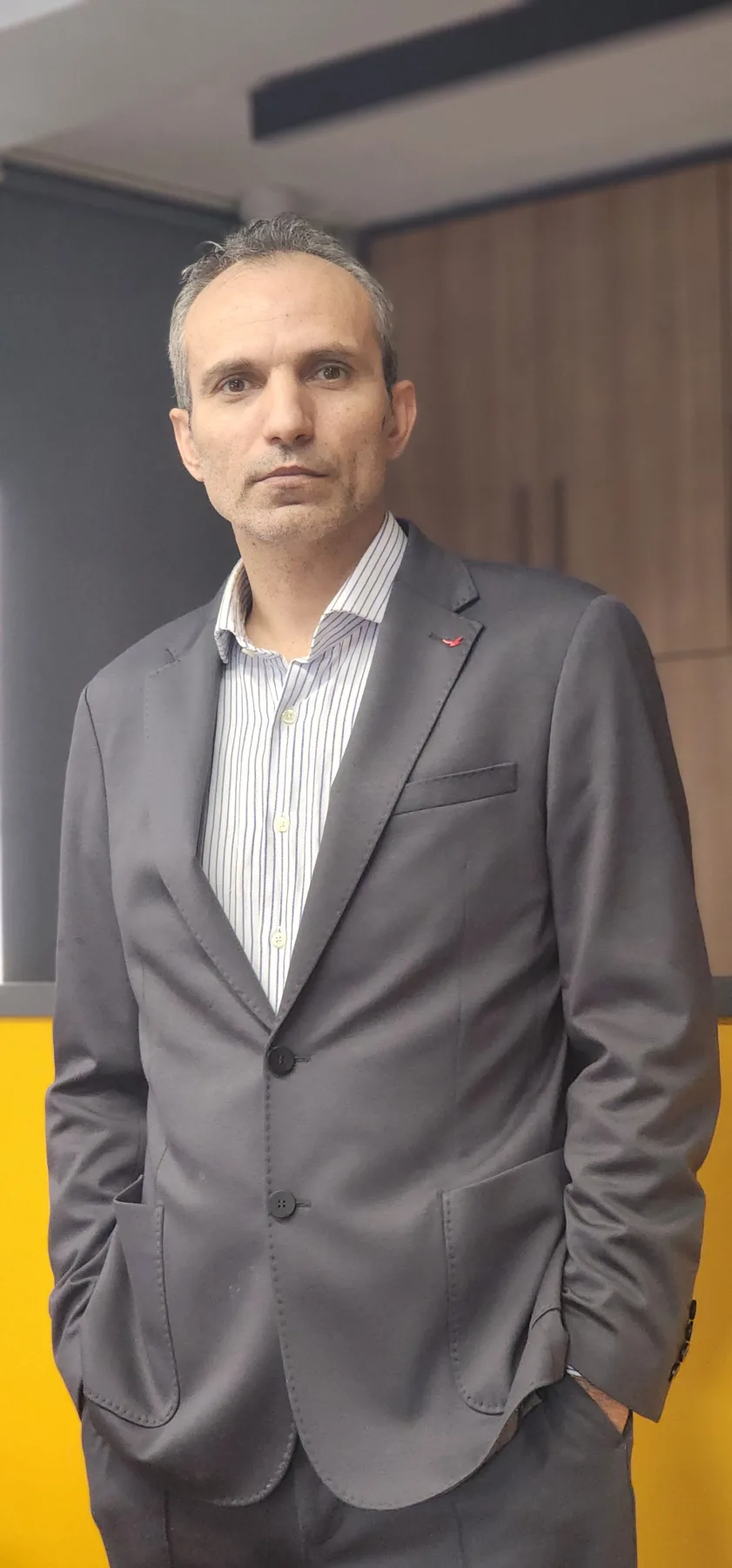 Galip Arduç'un Royal Green iş yerinde, koyu gri takım elbisesi ve çizgili gömleğiyle, kurumsal ofis ortamında kendinden emin duruşunu yansıtan profesyonel portresi.