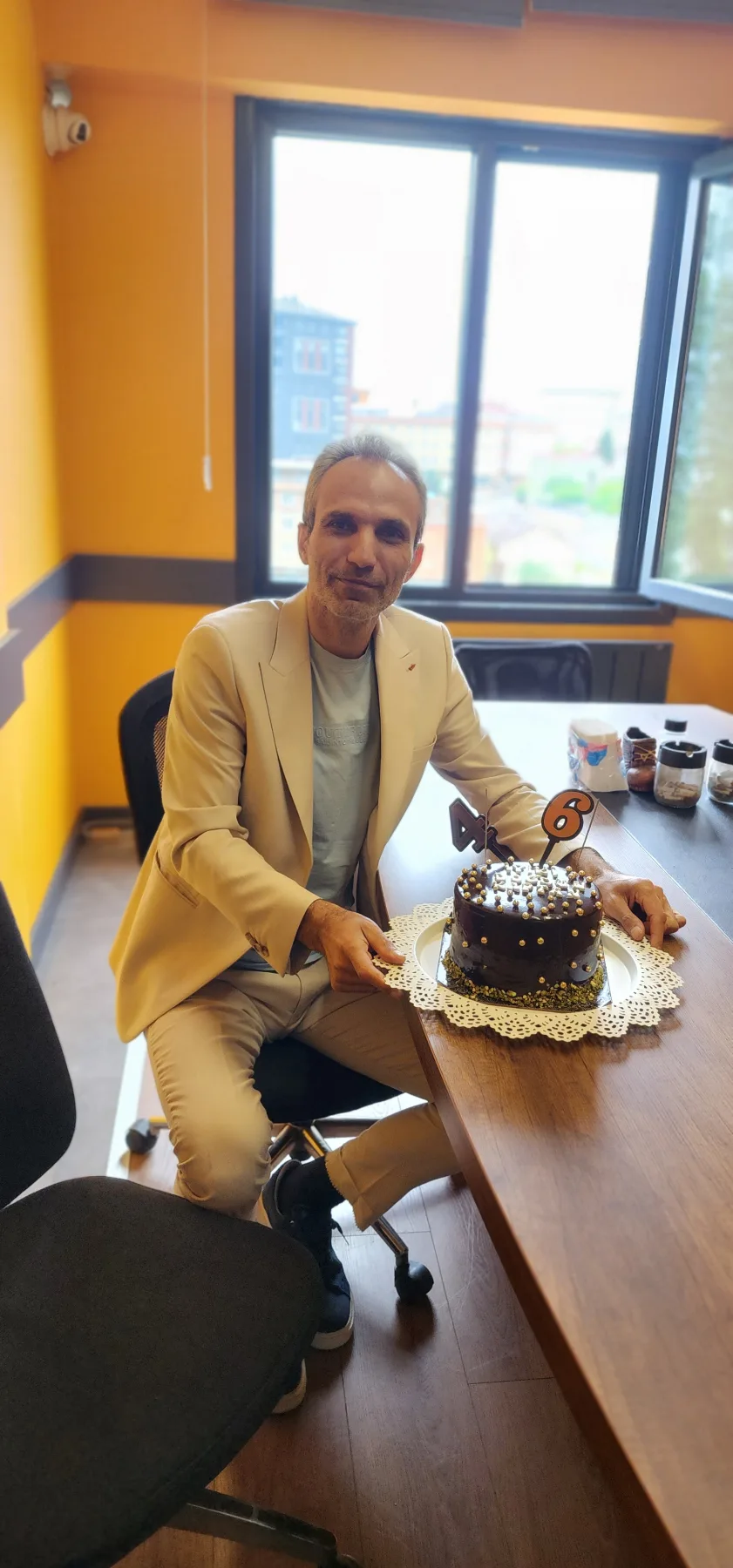 Galip Arduç, aydınlık bir ofiste masadaki üzerinde 46 rakamı bulunan pastanın yanında oturuyor.
