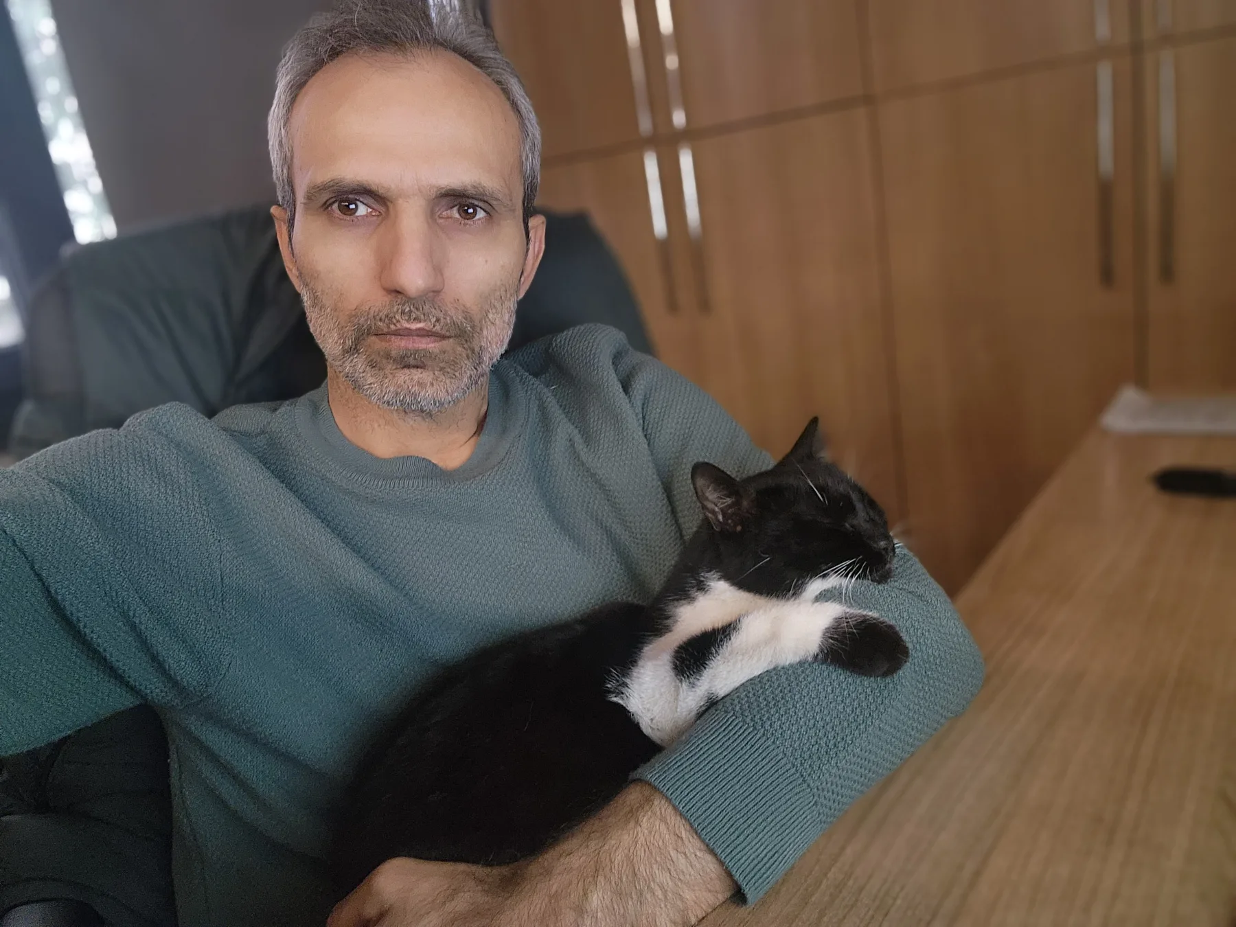 Galip Arduç’un fotoğraf arşivinden, yeşil kazaklı bir kişinin kucağında uyuyan siyah beyaz kedi.