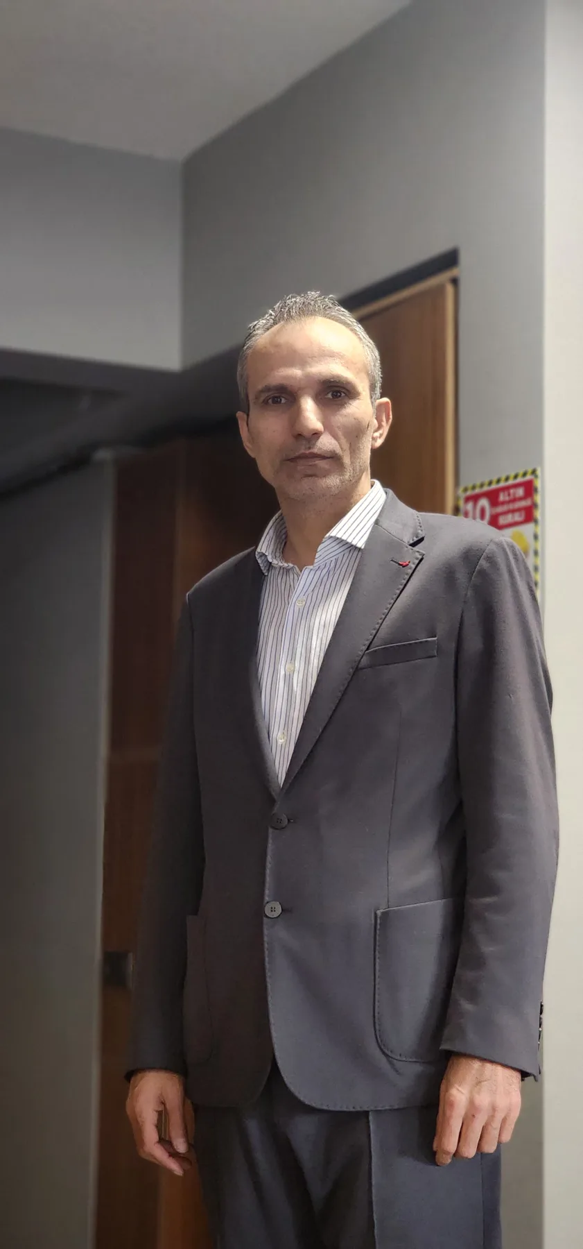 Galip Arduç'un Royal Green iş yerinde, koyu gri takım elbisesi ve çizgili gömleğiyle, modern ofis ortamında ciddi ve kendinden emin duruşunu yansıtan profesyonel portresi.