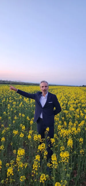 Galip Arduç’un Kırklareli’nde sarı kanola tarlasında, takım elbisesiyle ufku işaret ettiği doğal ve profesyonel portresi.