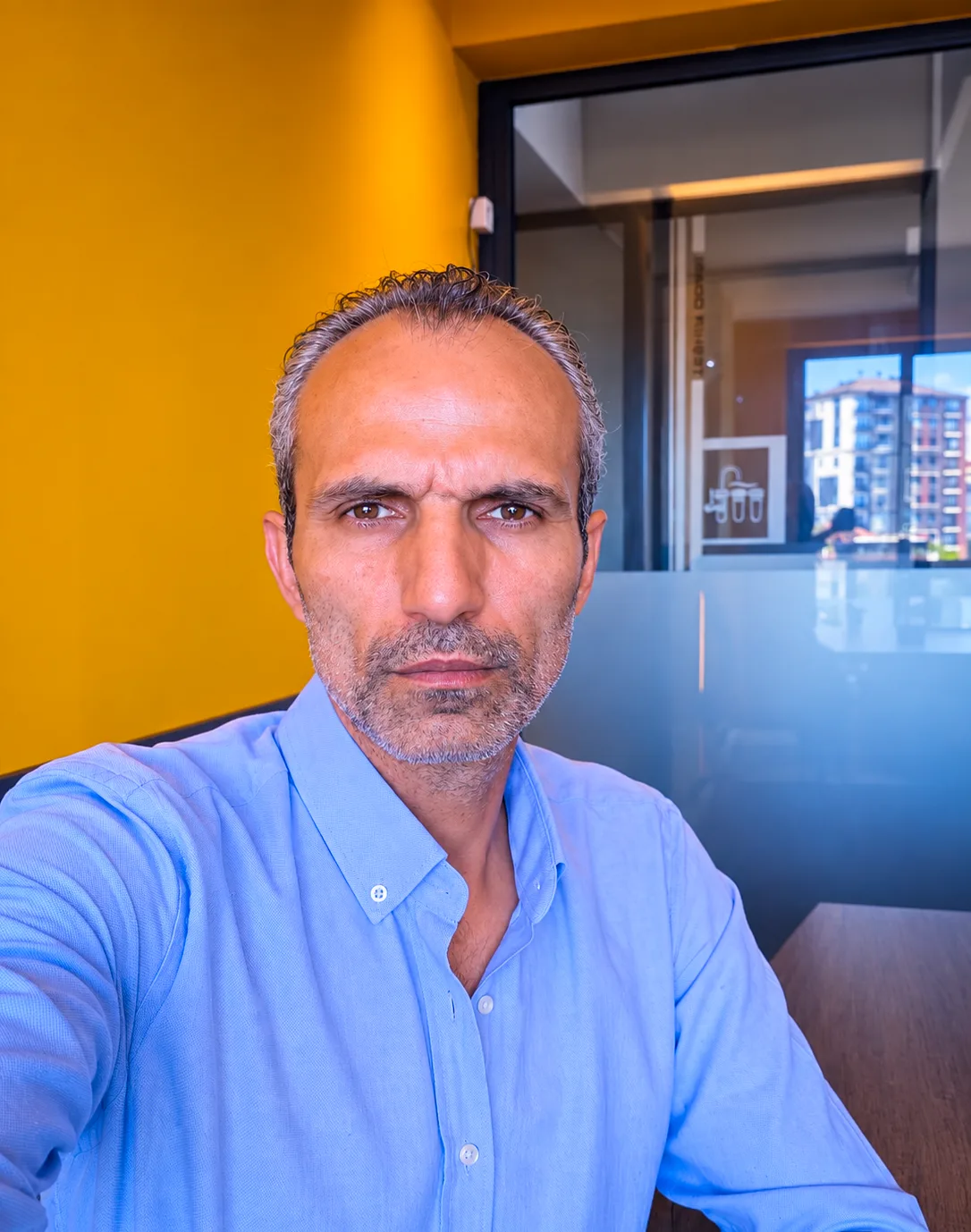 Galip Arduç’un iş ortamında mavi gömlekle kameraya doğrudan baktığı doğal ve ciddi portre fotoğrafı.