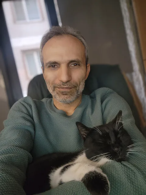 Galip Arduç’un fotoğrafında, yeşil kazaklı bir kişi kucağında siyah beyaz bir kediyle oturuyor.
