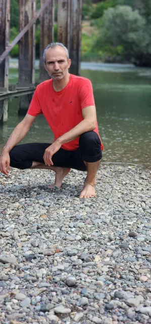 Galip Arduç’un fotoğraf arşivinden, çakıllı kıyıda kırmızı tişörtle çömelmiş bir kişinin ve arkasındaki ahşap köprünün görünümü.