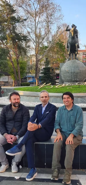 Galip Arduç’un fotoğraf arşivinden, bir anıtın önünde yan yana oturan üç kişinin açık havadaki karesi.