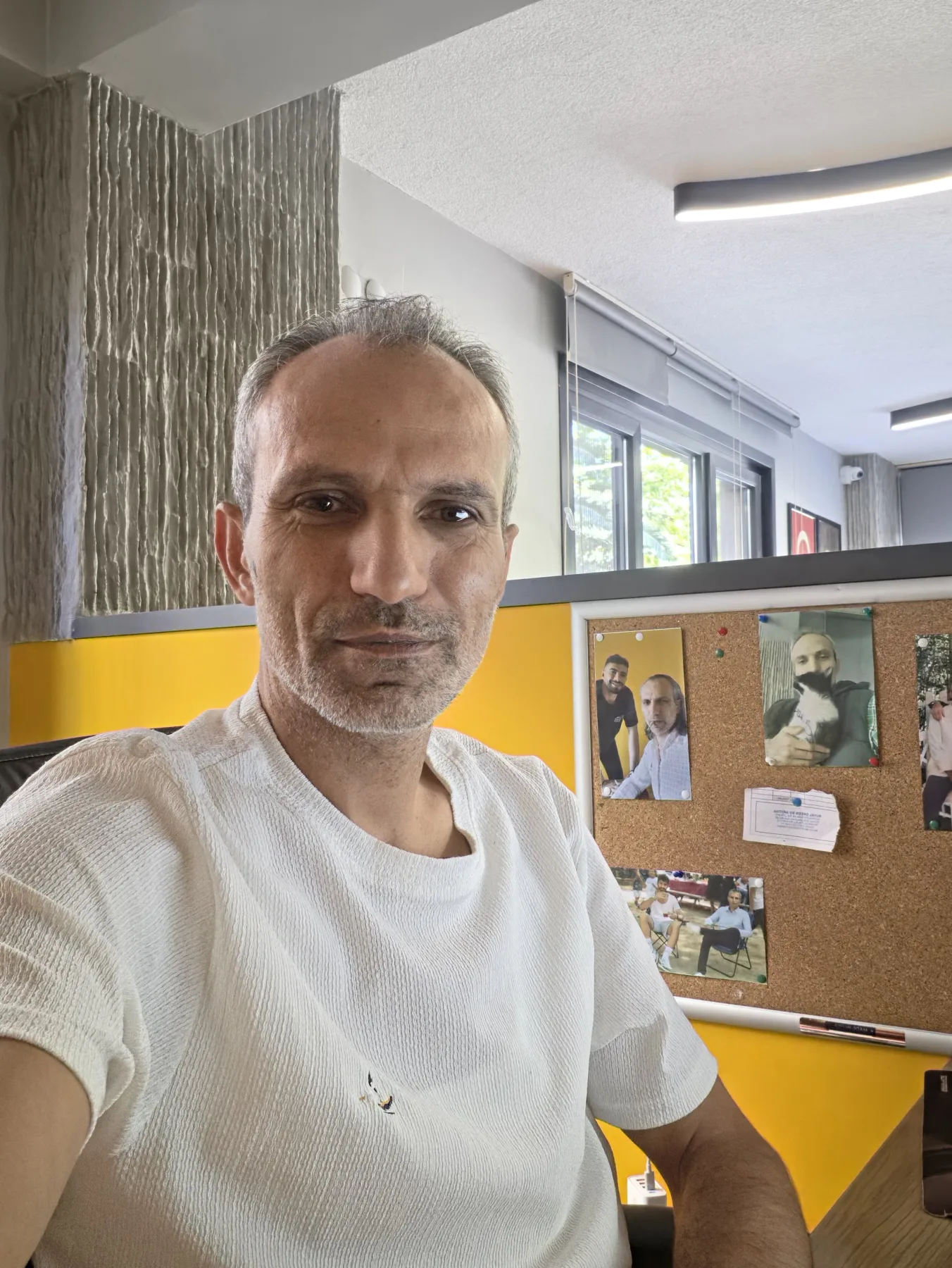 Galip Arduç’un fotoğraf arşivinden, aydınlık bir çalışma alanında beyaz tişörtlü bir kişinin çektiği özçekim.