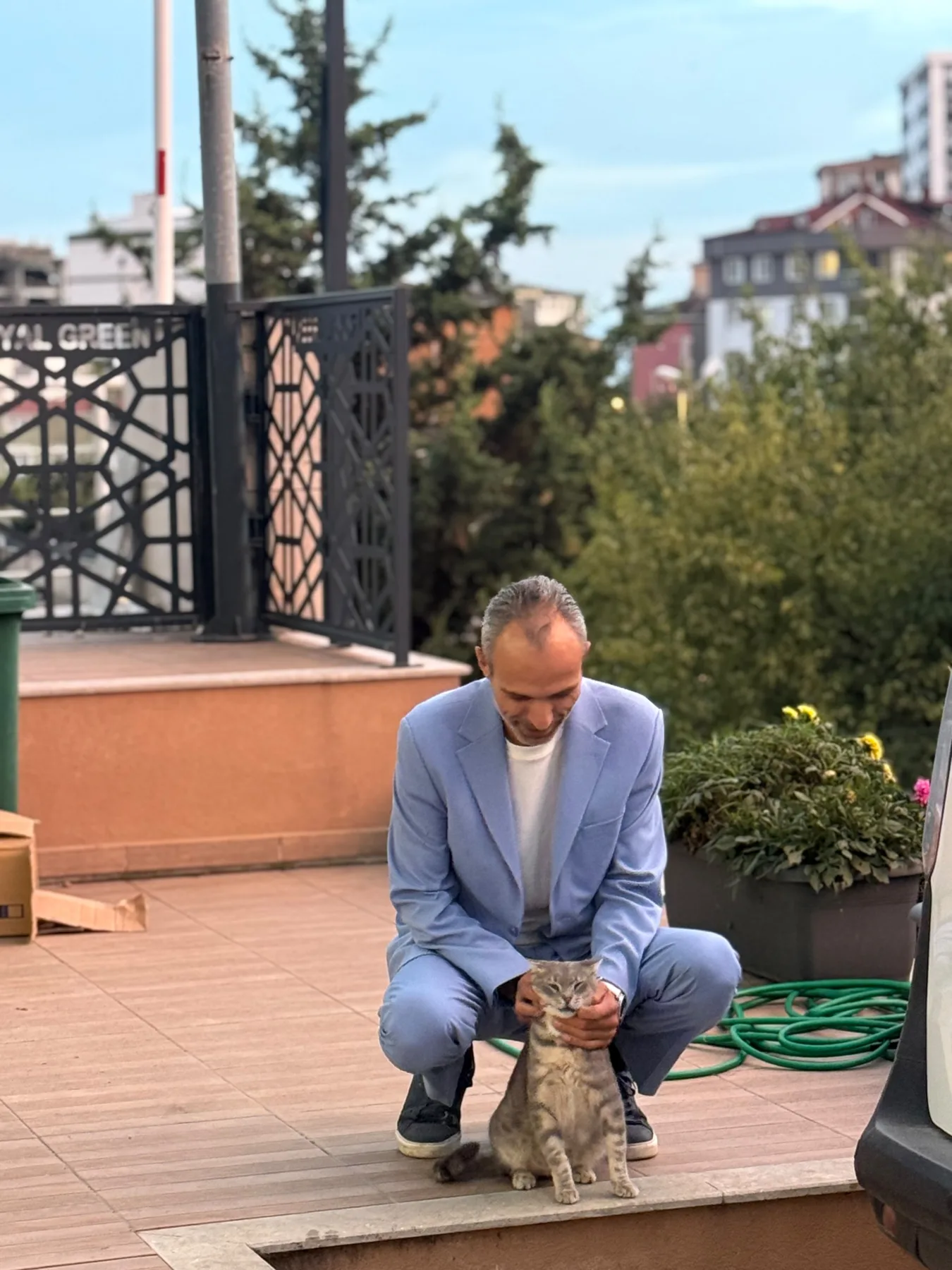Galip Arduç’un açık havada mavi takım elbisesiyle bir kediyi severken çekilmiş doğal portresi.